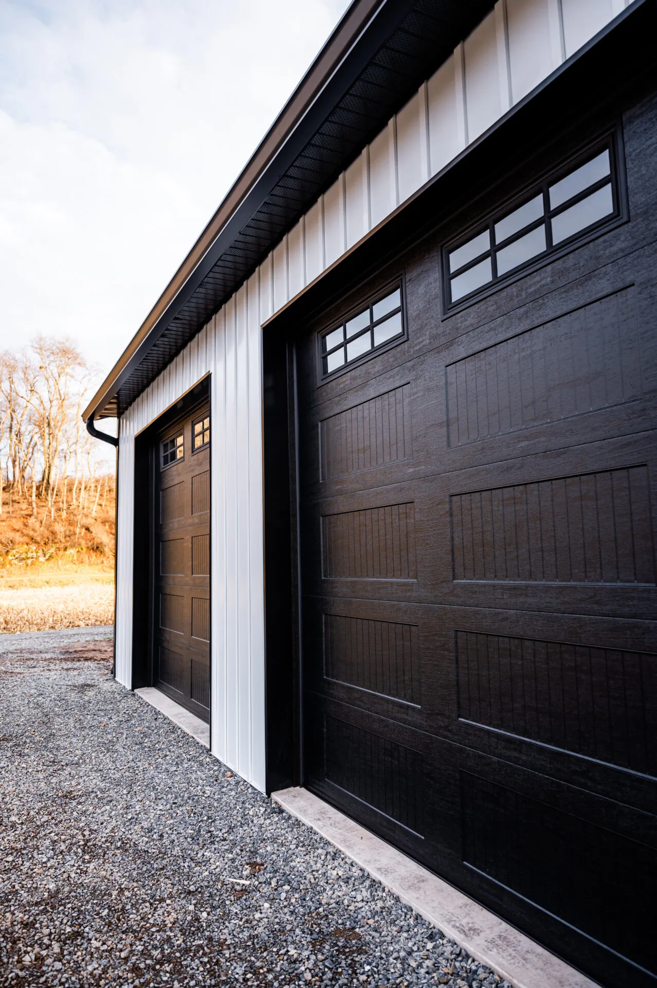Close view of two black wood-grain overhead doors with window rows, set into white vertical siding under a charcoal roof
