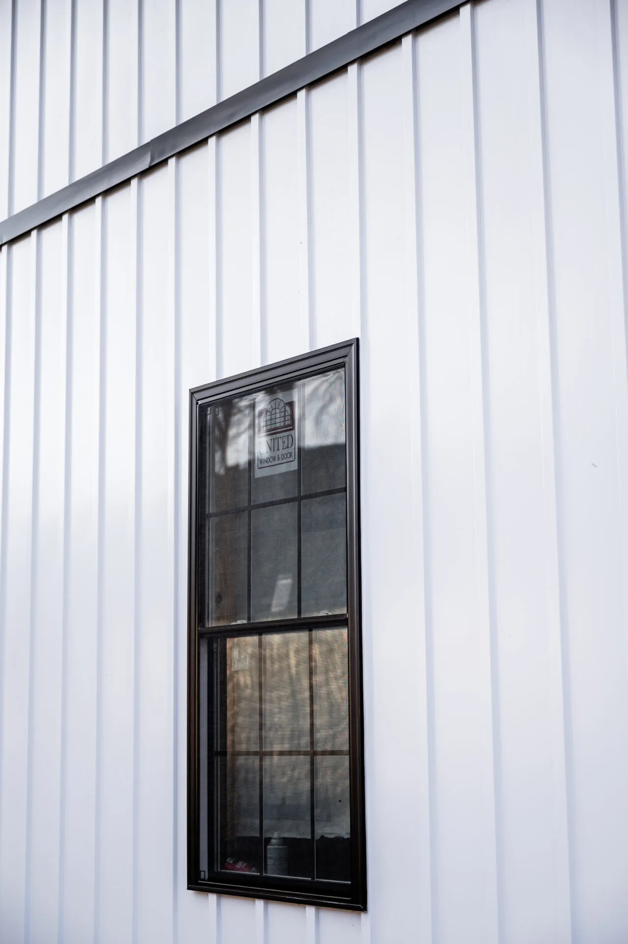 Close view of white vertical metal siding with a black-framed double-hung window and black trim